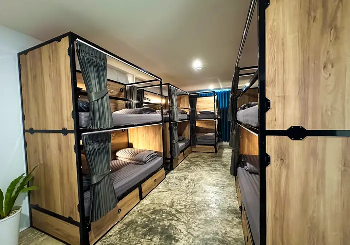 Aisle lined with wooden bunks, plant and teal curtain