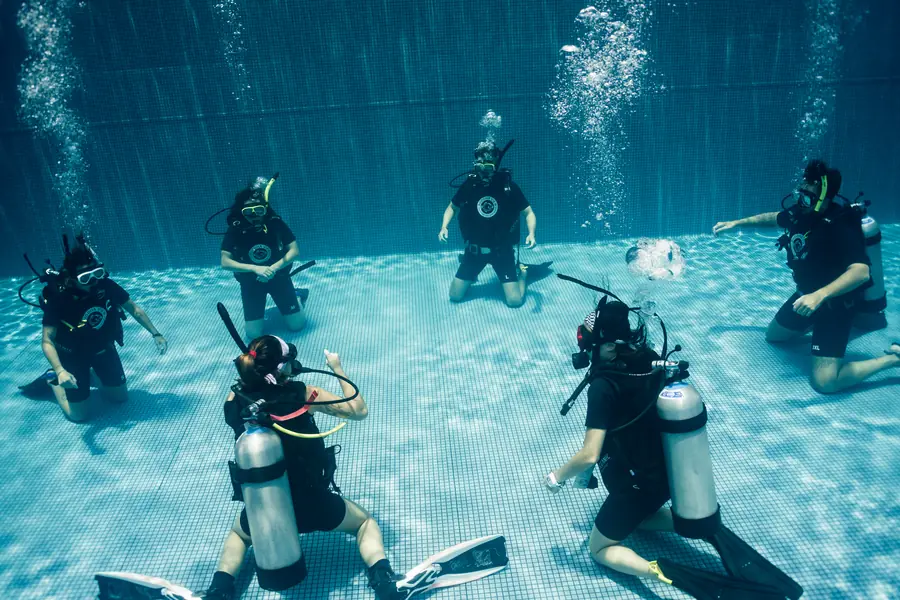 An instructor and five students kneeling on the bottom of the training pool