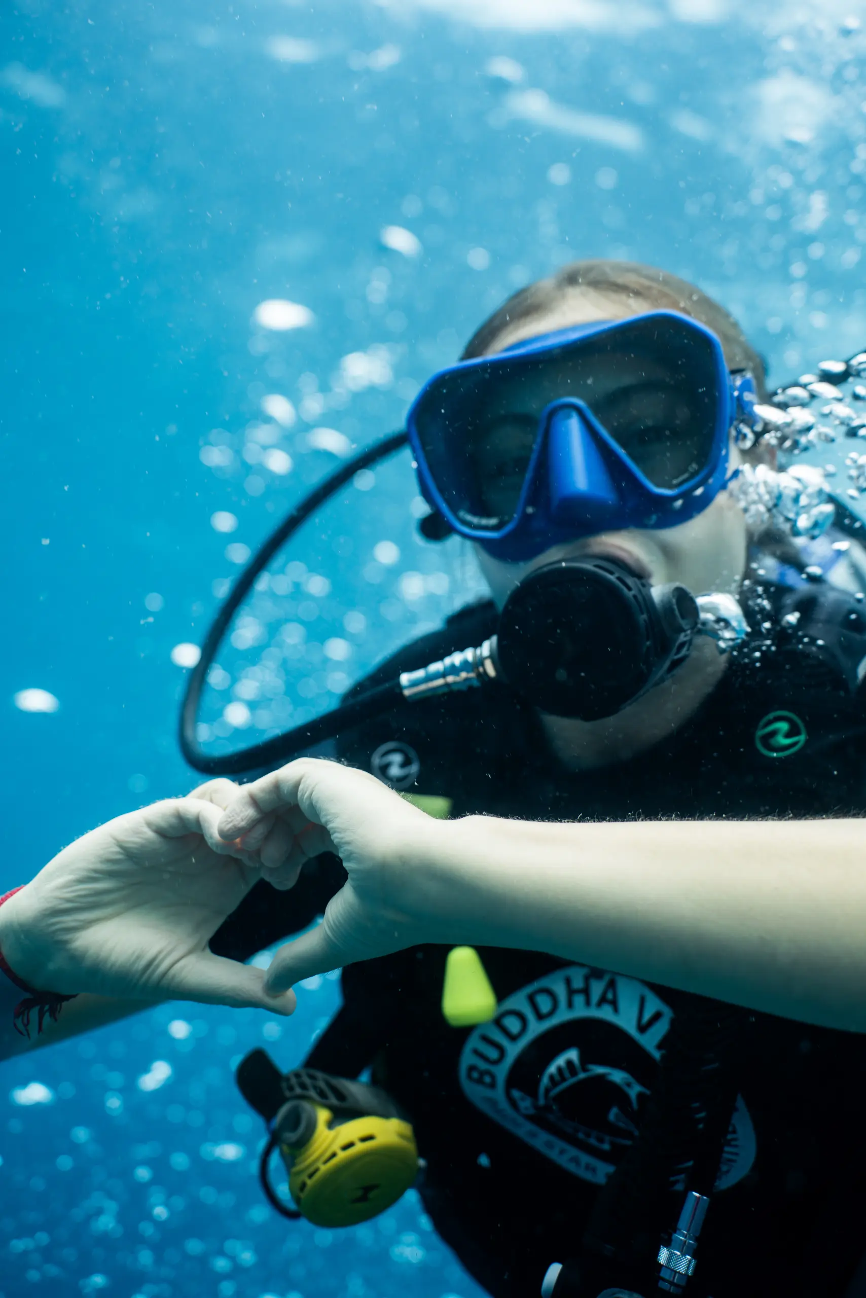 Two divers smiling at the camera above a sea anemone, an instructor just behind them