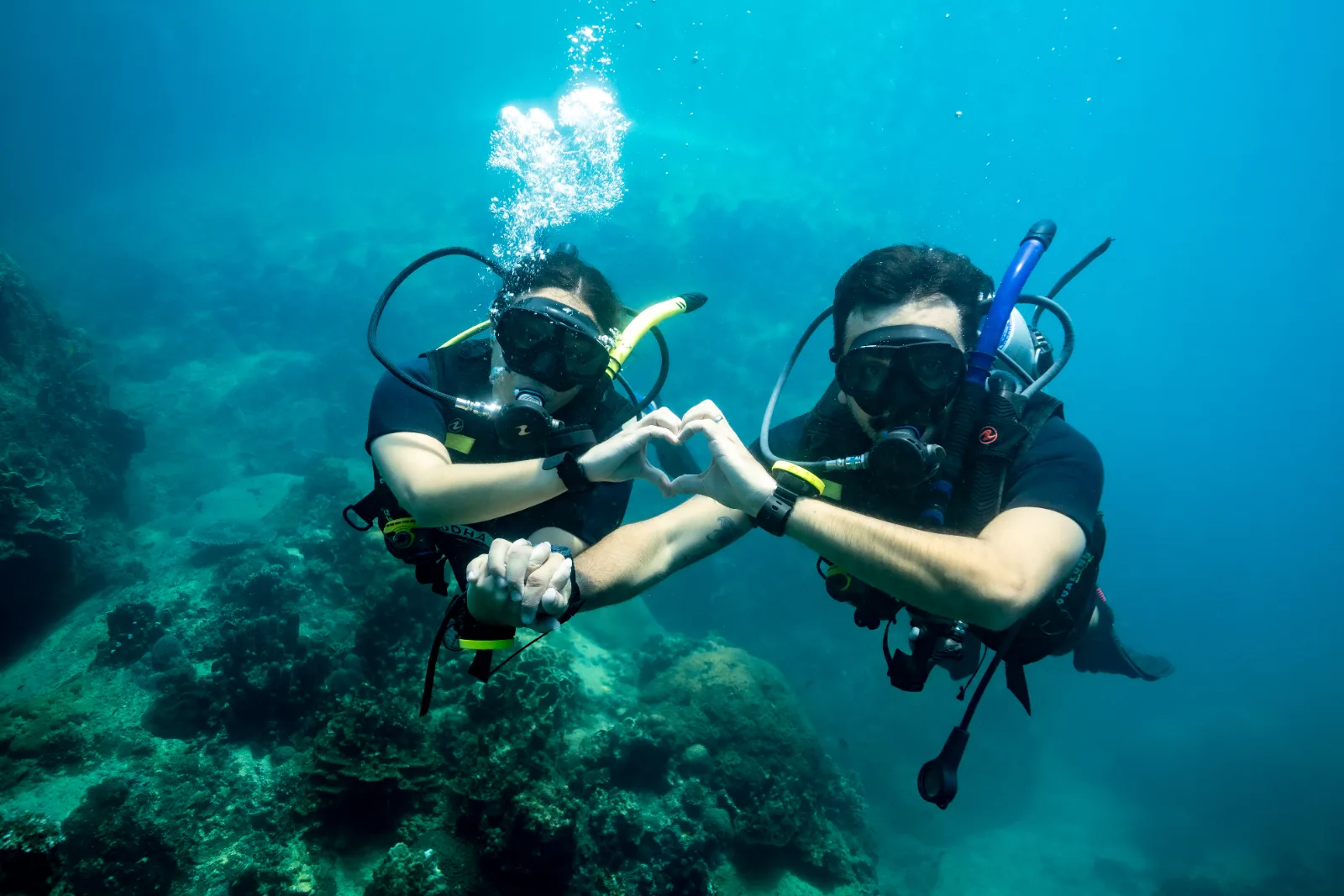 Two certified divers making a heart with their hands above the reef