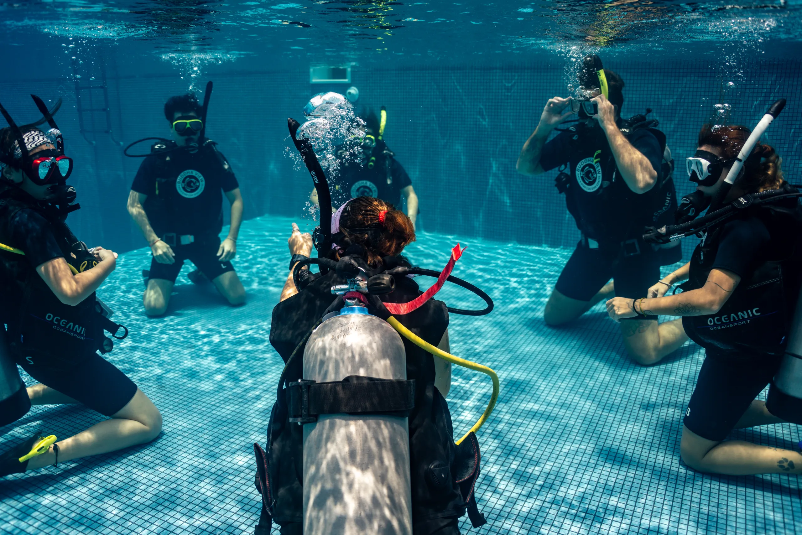 Divers kneeling in a circle on the pool floor, reviewing skills with their instructor